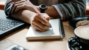 Person sitting at a desk writing out a project ‘to do’ list