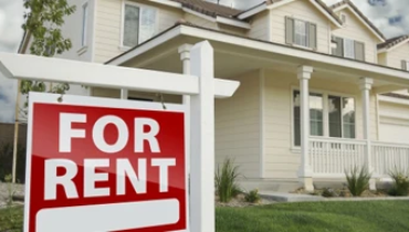 Red, right facing for rent real estate sign in front of beautiful house.